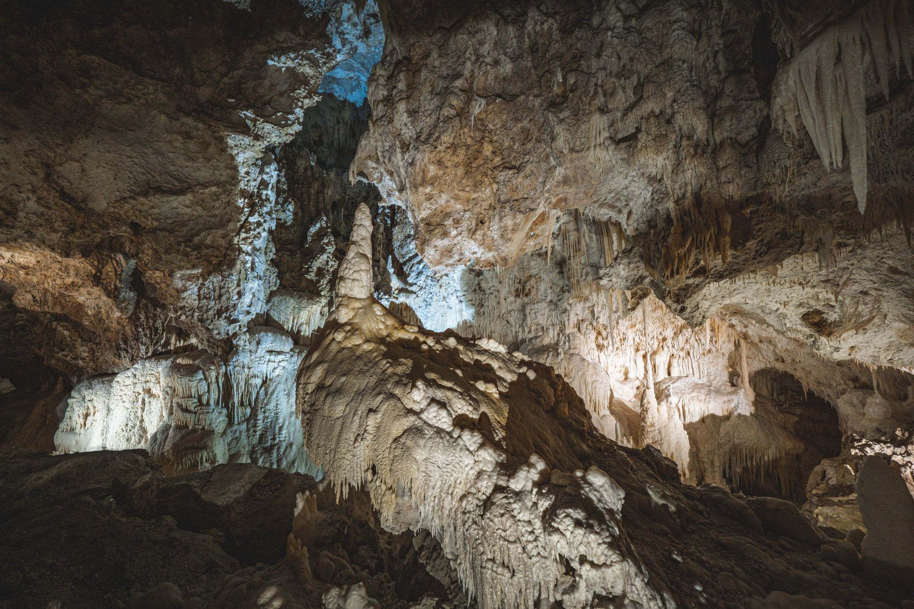 Intérieur d’une grotte calcaire éclairée, avec une grande stalagmite au centre, des stalactites et des parois rocheuses.